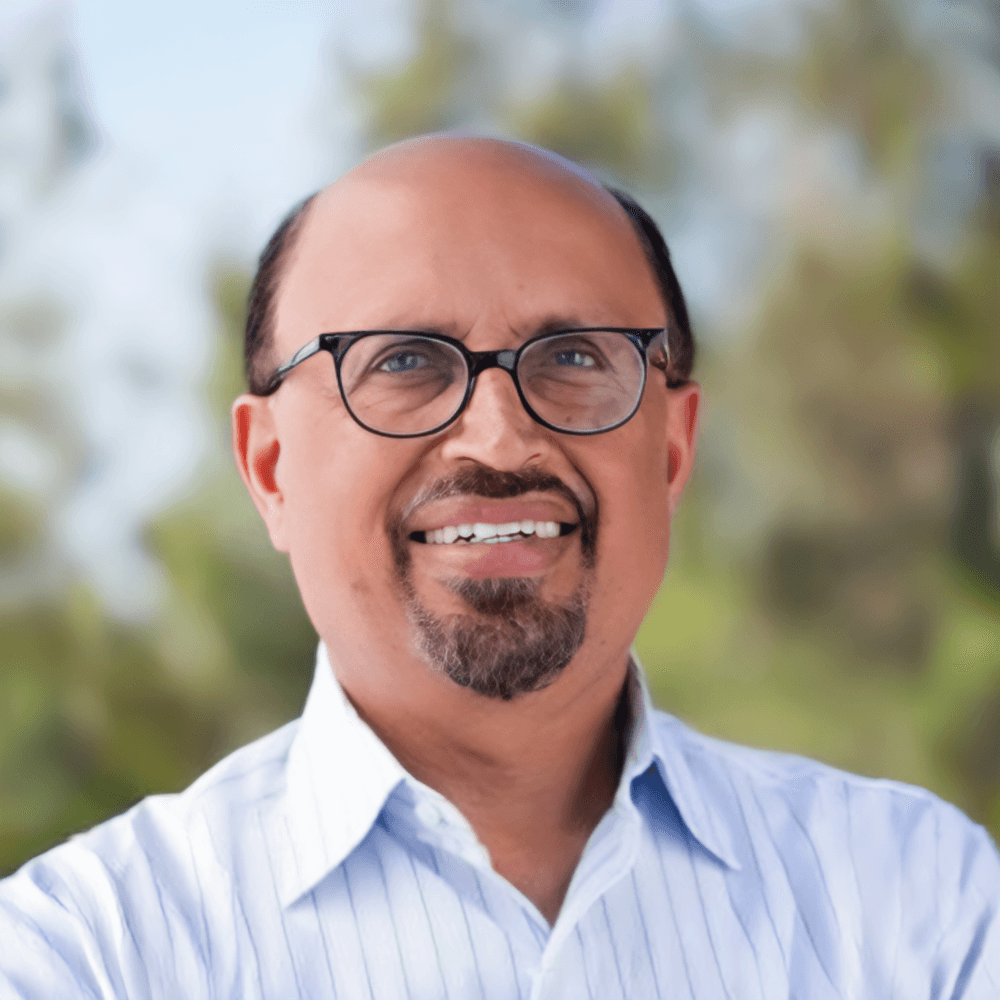 Ajay Chopra wearing glasses and a blue shirt with a white collar.